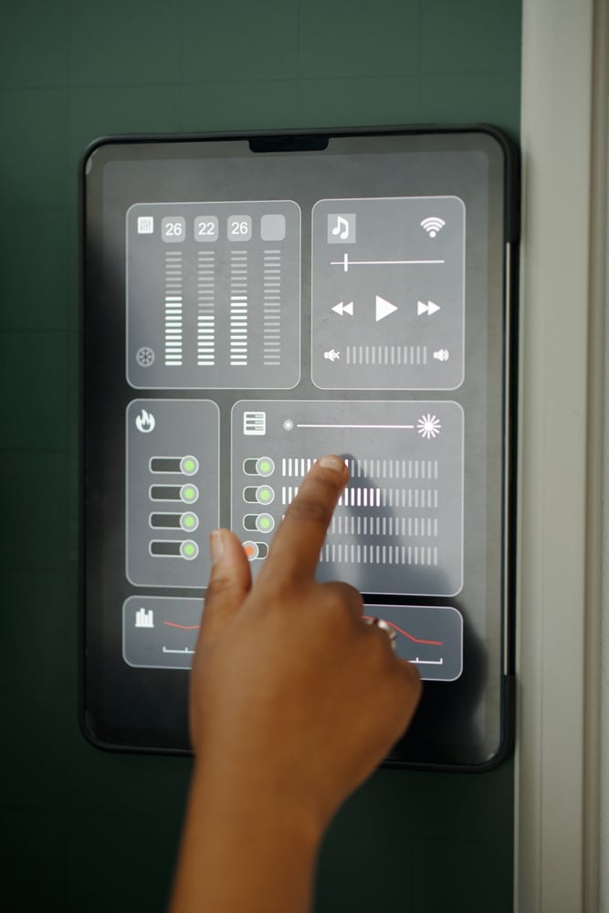 Domotique : contrôle tactile d'une maison intelligente Main réglant l'éclairage sur un écran domotique avec contrôles de température et musique d'une maison connectée.