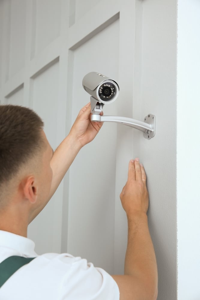 Installation de caméra de surveillance par un expert Technicien ajustant une caméra de surveillance grise installée sur un mur blanc intérieur.