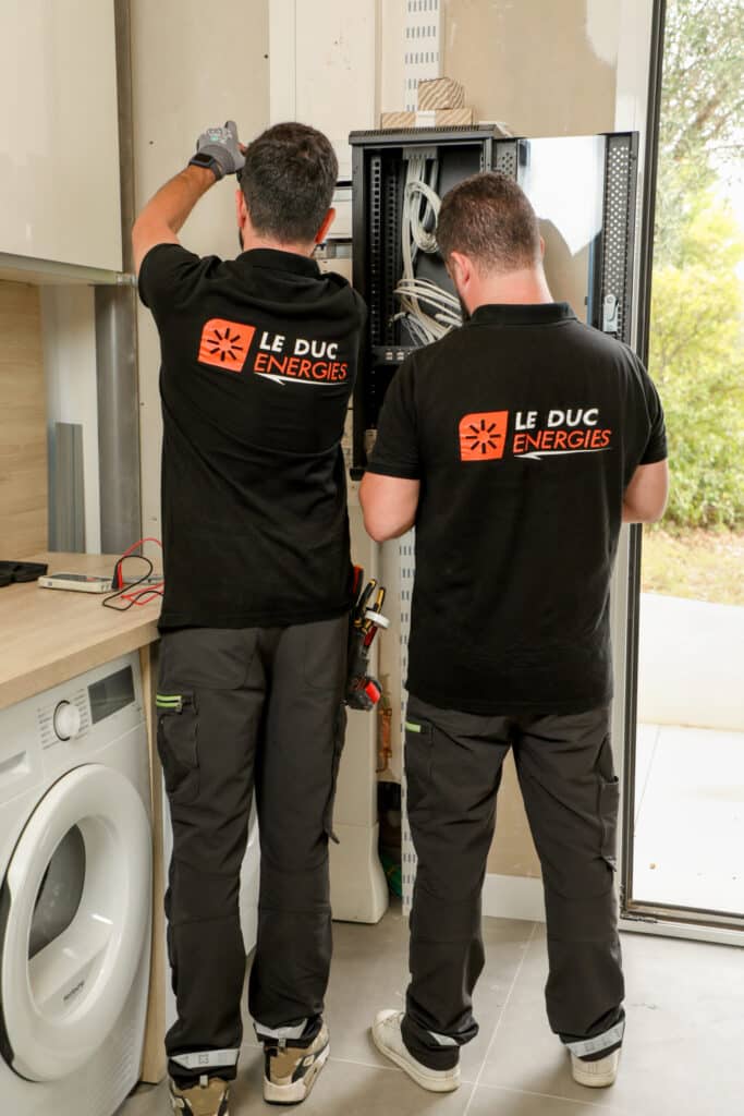 Installation électrique et réseau par Le Duc Energies Deux techniciens de Le Duc Energies installant un tableau électrique et du câblage réseau dans un local technique.