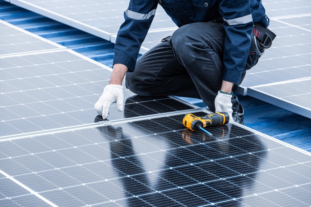 Installation de panneaux solaires par un technicien qualifié Technicien installant des panneaux solaires sur un toit bleu avec une visseuse électrique jaune.