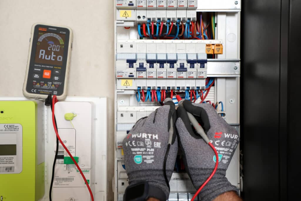 Maintenance tableau électrique : test au multimètre Électricien testant un tableau électrique avec un multimètre numérique affichant 20.0 Auto et disjoncteurs Gewiss.