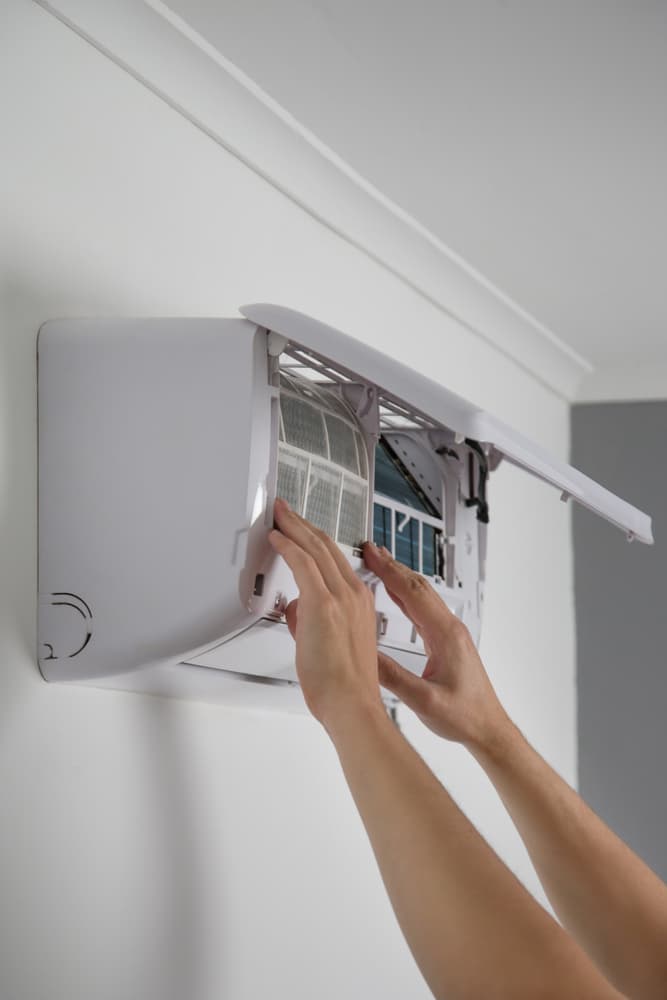 Mains retirant le filtre d'un climatiseur mural blanc pour un entretien régulier de l'appareil.