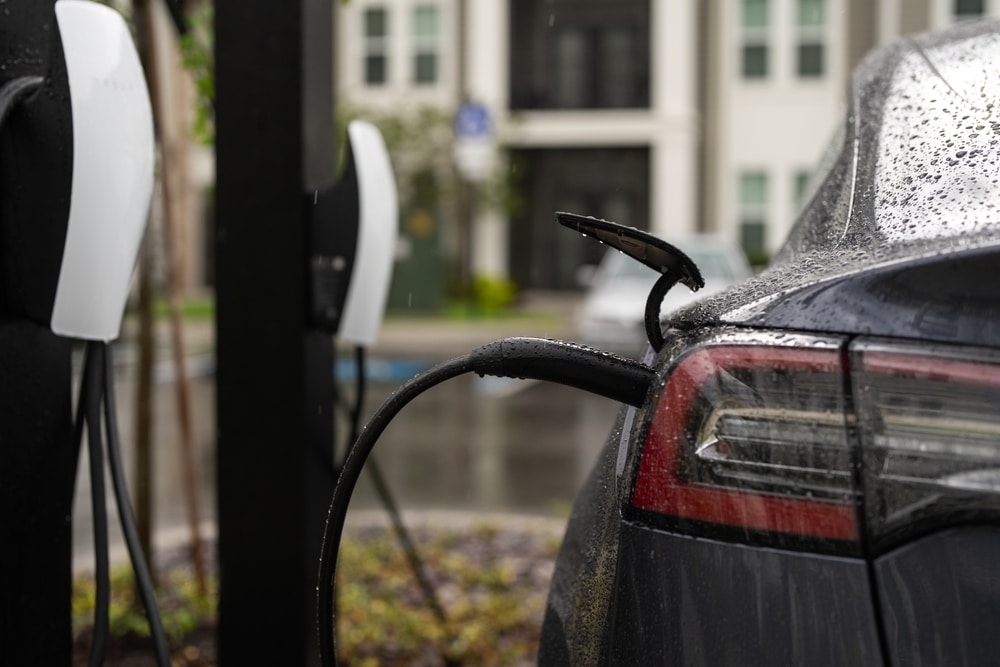Recharge de Tesla sous la pluie : Borne électrique VE Tesla noire en charge sous la pluie, câble branché à une borne électrique extérieure.