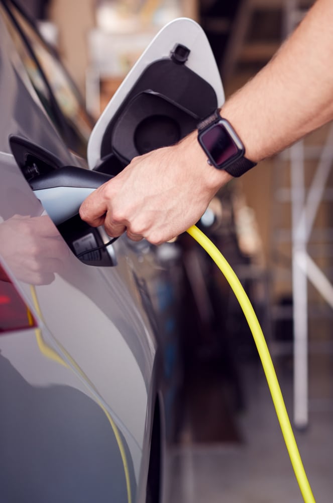 Recharge de Voiture Électrique à Domicile : Guide Pratique Main branchant un câble jaune sur une voiture électrique grise pour une recharge à domicile dans un garage.