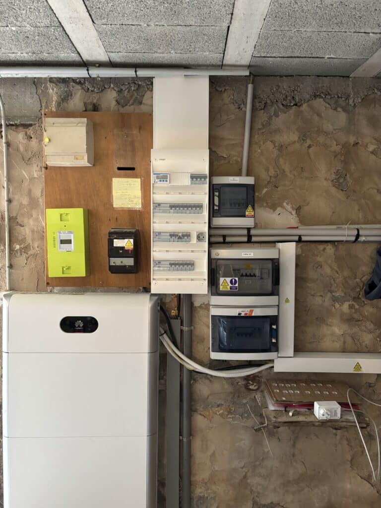 Panneau électrique avec compteur Linky, batterie solaire Huawei et coffrets de disjoncteurs sur mur en pierre brute.